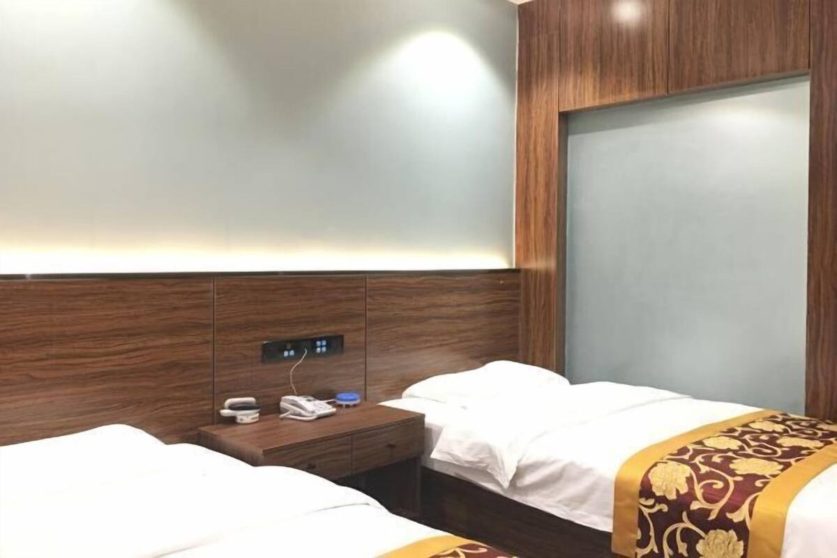 Ein Hotelzimmer mit zwei Betten, einem hölzernen Kopfteil, einem Nachttisch mit Telefon und Lampe sowie einer Wandleuchte.