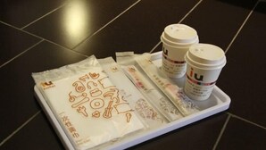 A tray with two coffee cups and a set of stickers on a dark tiled floor. - IU Hotel (Fengdu County)