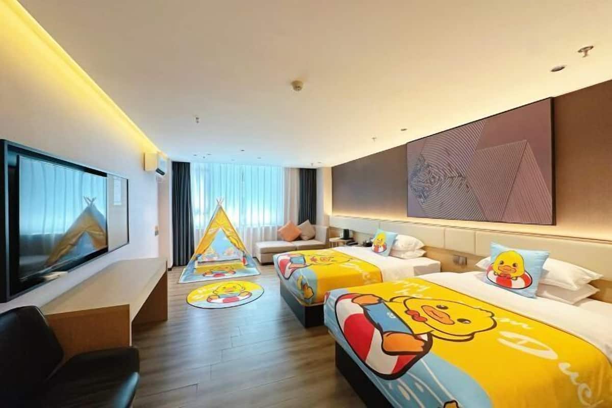 A hotel room with two beds, a TV, a desk, and a large window.