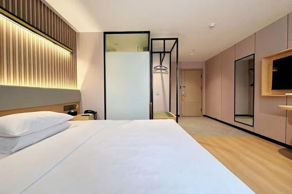 A modern hotel room with a large bed, a bedside table, a TV, and a mirror.