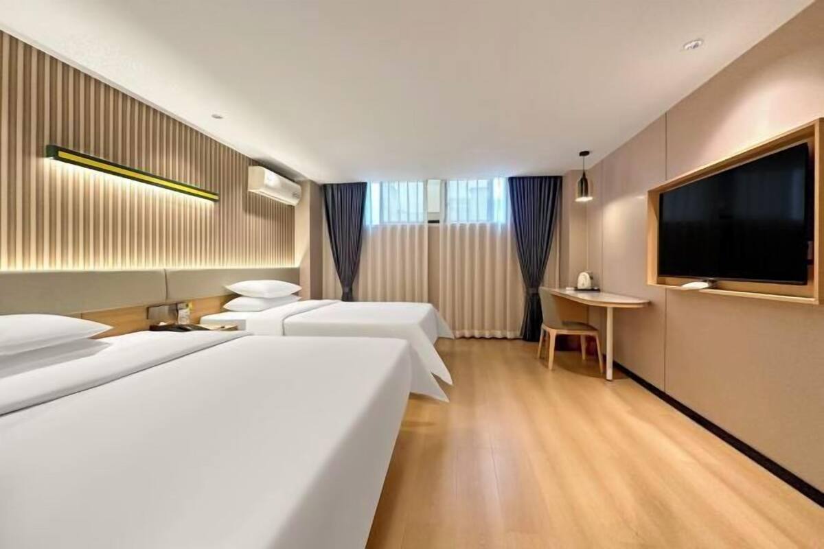A hotel room with two beds, a TV, a small table, and a window with curtains.