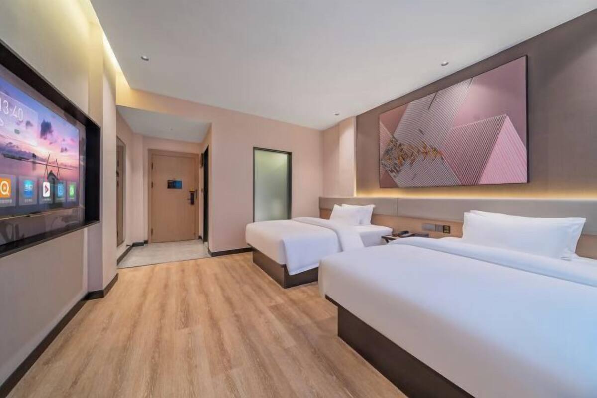 A hotel room with a large bed, two smaller beds, a TV displaying a sunset, and a modern abstract painting on the wall.