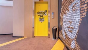 A hallway with a yellow elevator door, a trash bin, and a large poster on the wall. - IU Hotel (Chongqing Fengdu Ghost City) (Fengdu County)