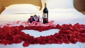 A bed with rose petals arranged in a heart shape, a bottle of wine, and a glass of wine on the bed. - IU Hotel (Fengdu County)