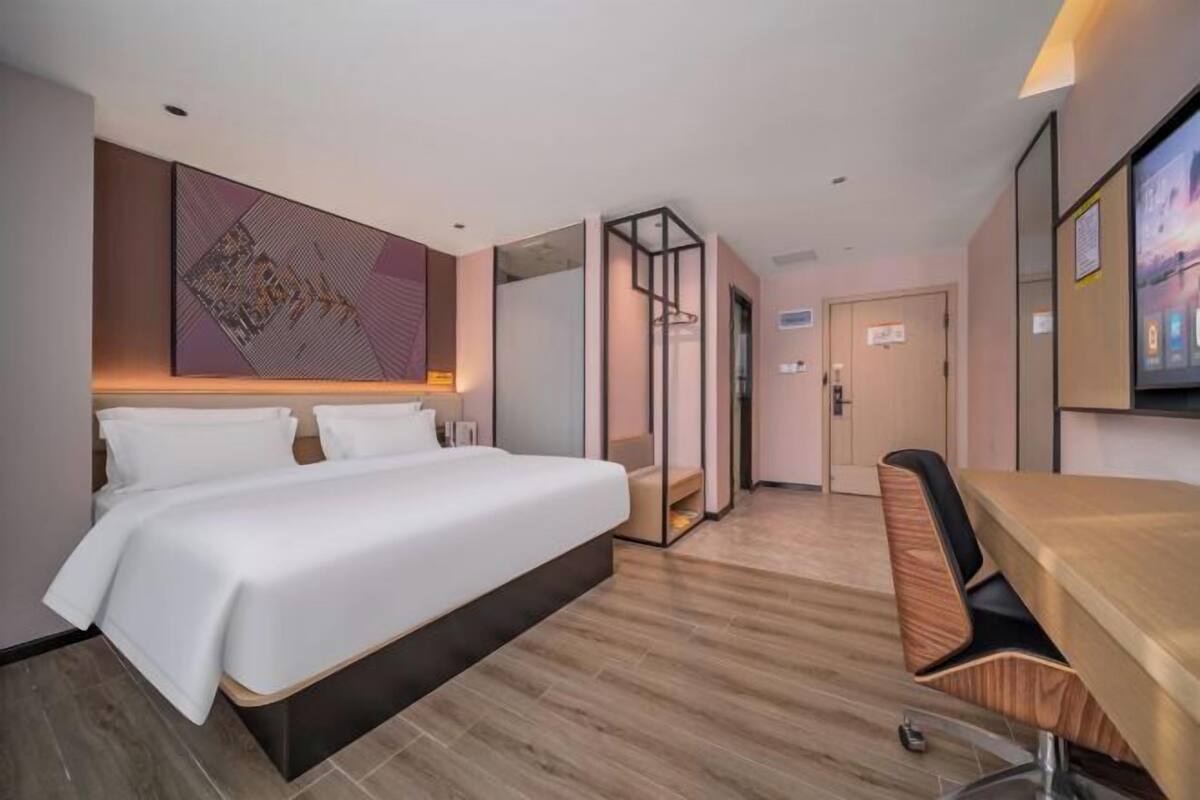 A modern hotel room with a large bed, a desk, and a seating area.