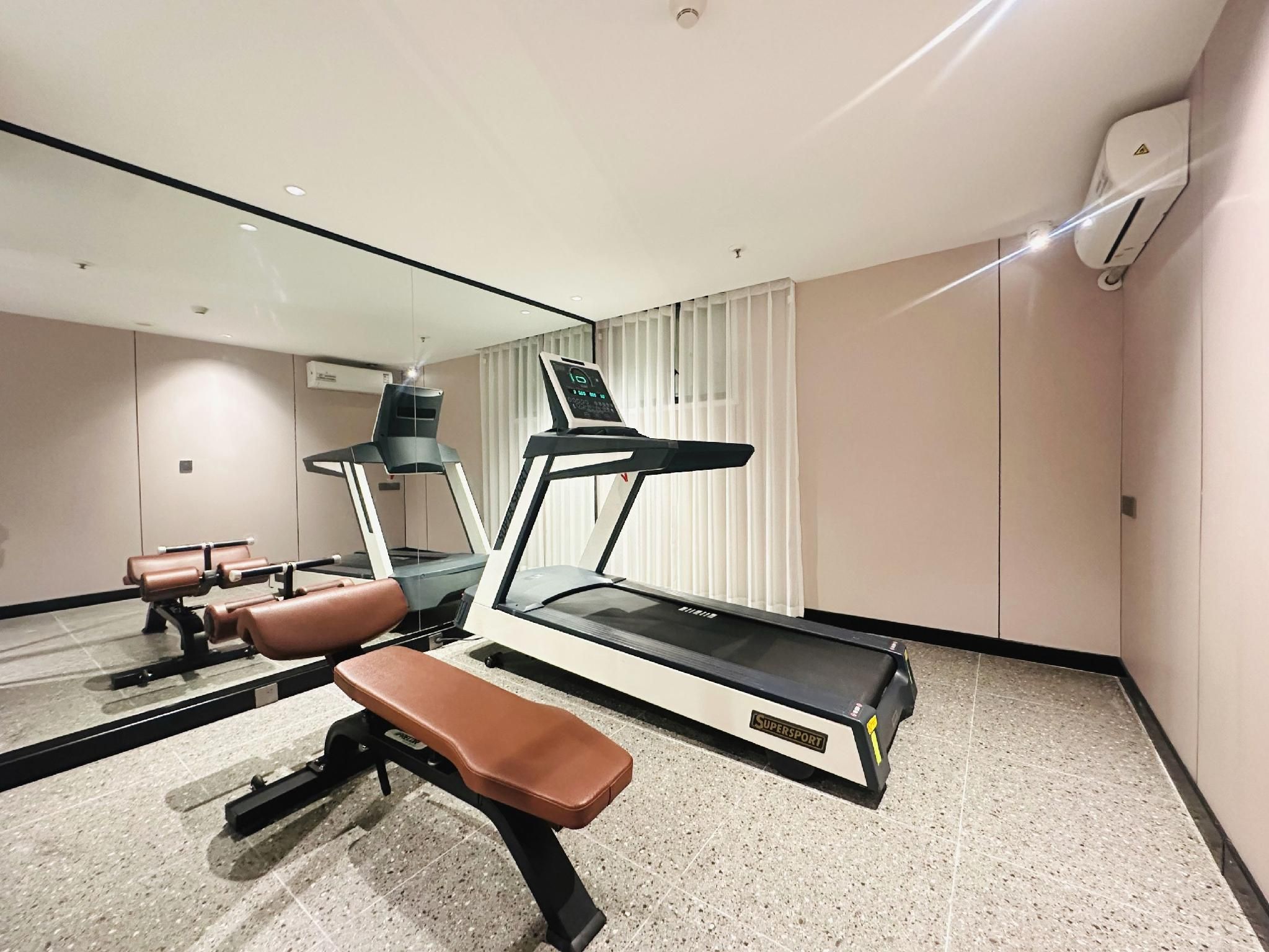 Un gimnasio moderno con cinta de correr, banco y máquinas de pesas.