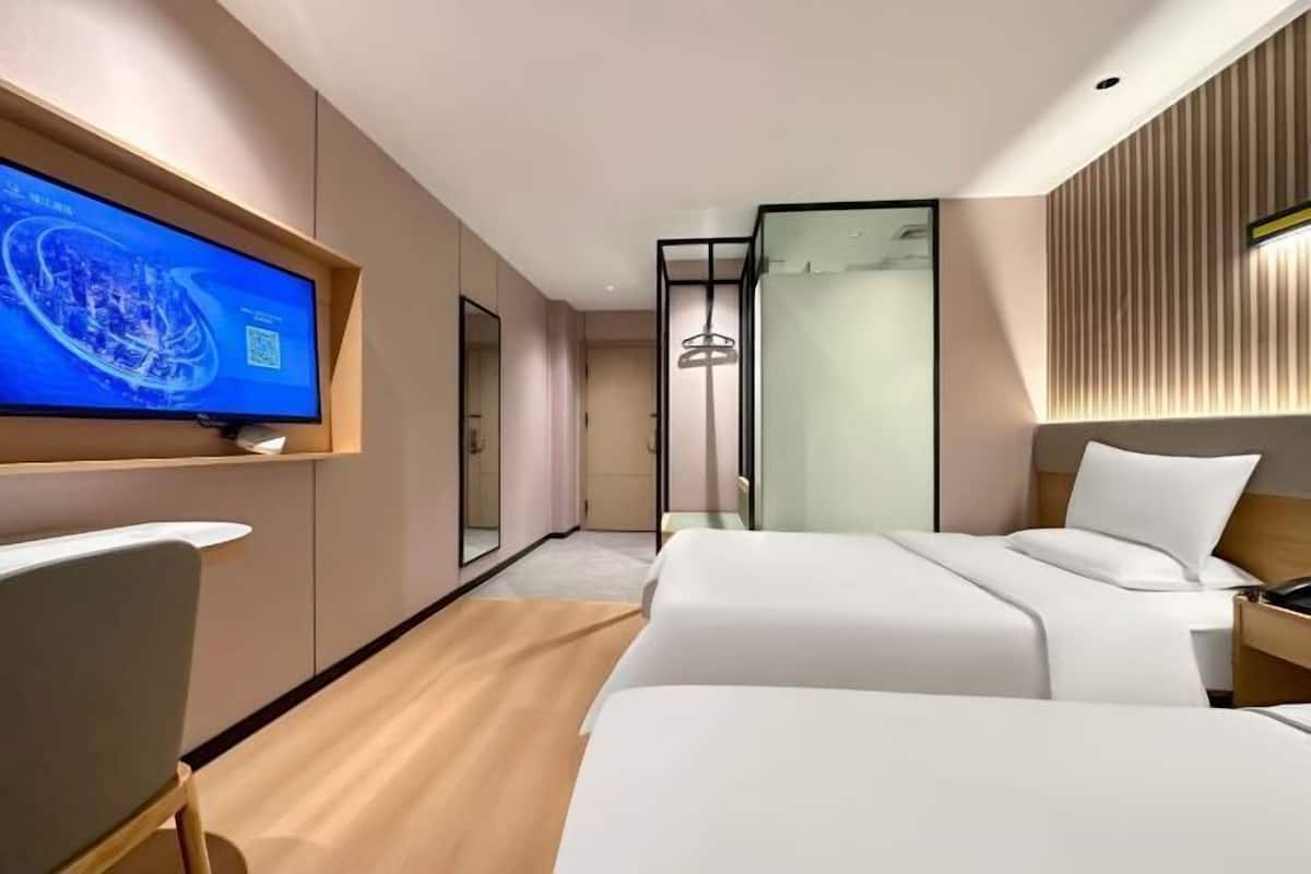 A modern hotel room with a large flat-screen TV, two beds, a desk, and a chair.