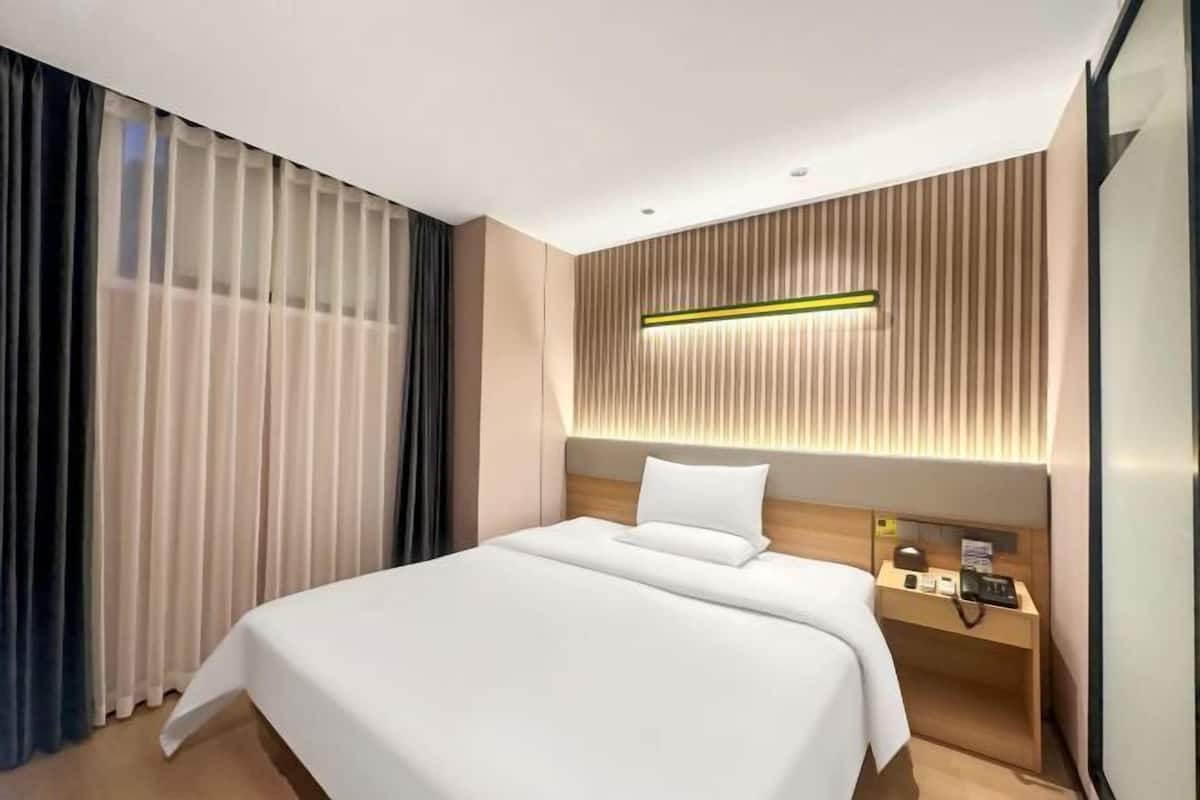 A modern hotel room with a large bed, a bedside table with a lamp, and a wall-mounted light fixture.