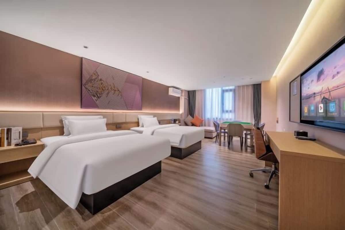 A hotel room with two beds, a desk, a chair, and a TV.