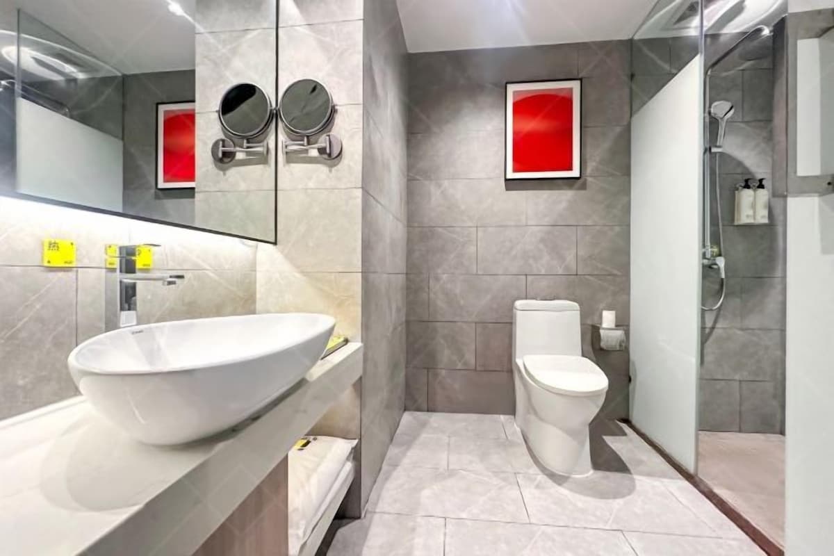 A modern bathroom with a large vessel sink, a toilet, a shower, and a mirror with two round mirrors above it.