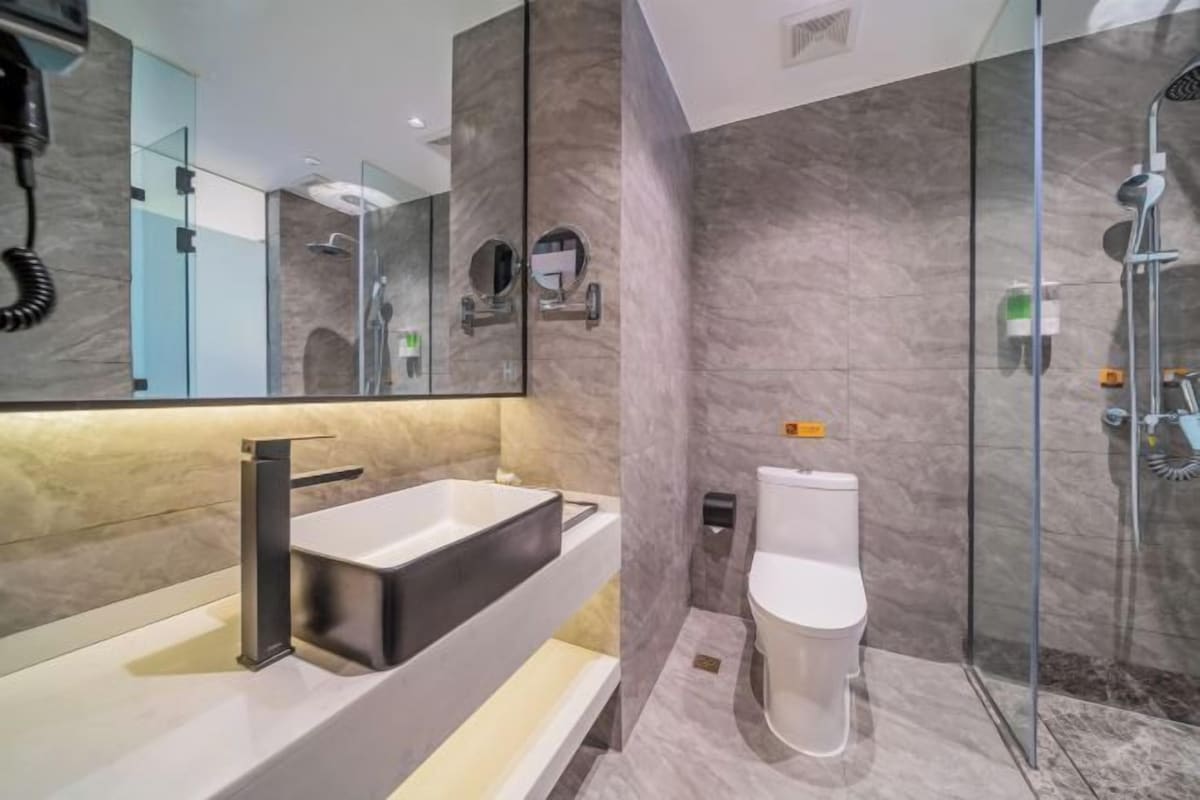 A modern bathroom with a large mirror, a black sink, a toilet, and a glass-enclosed shower area.