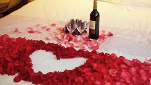 A bed with rose petals arranged in a heart shape, two wine glasses, and a bottle of wine. - IU Hotel (Fengdu County)