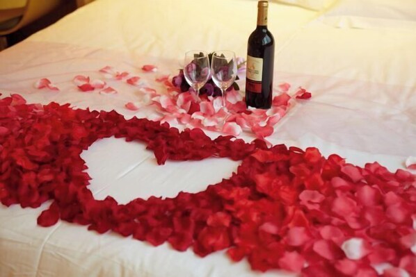 A bed with rose petals arranged in a heart shape, two wine glasses, and a bottle of wine. - IU Hotel (Fengdu County)