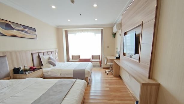 A hotel room with two beds, a desk, a chair, a TV, and a large window.