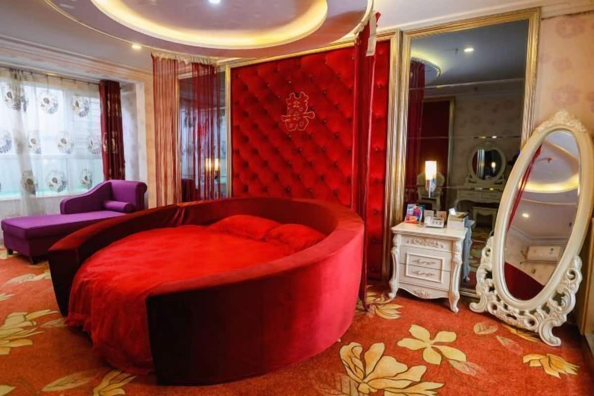 A luxurious bedroom with a red velvet bed, a vanity with a mirror, and a red upholstered chair.