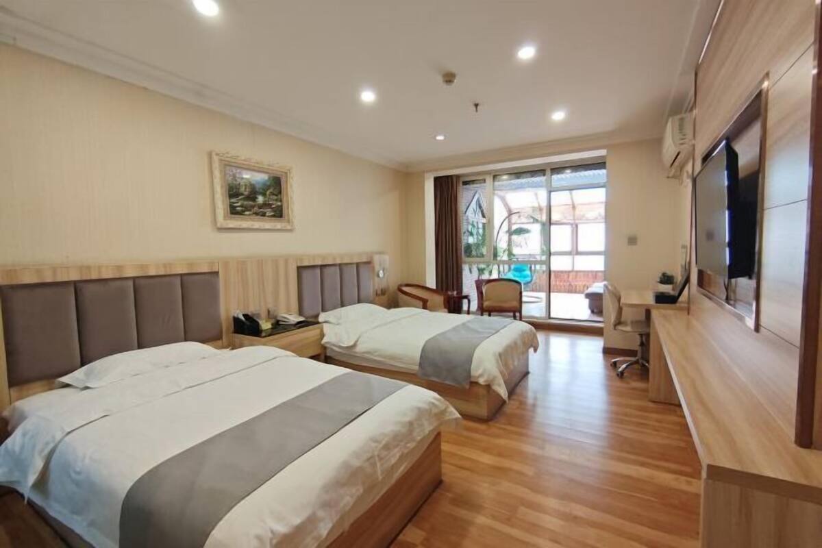 A hotel room with two beds, a desk, a chair, a TV, and a window with a view of the outside.