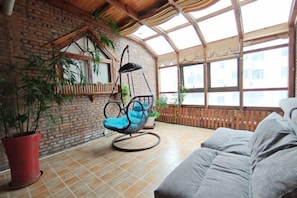 A cozy room with a brick wall, a hanging chair, a sofa, and large windows.