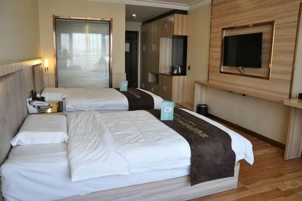 A hotel room with two beds, a TV mounted on the wall, and a wardrobe.