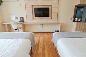 A hotel room with two beds, a desk, a TV mounted on the wall, and a cabinet.