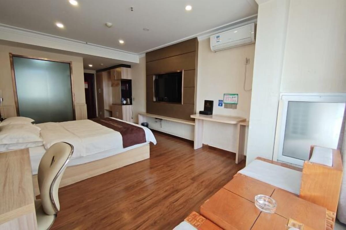 A hotel room with a bed, a desk, a chair, a TV, and an air conditioning unit.
