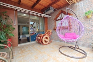 An outdoor seating area with wicker chairs and a hanging chair, a brick wall, and a wooden ceiling.