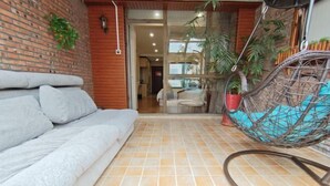 A room with a grey sofa, a hanging chair with a blue cushion, and a tiled floor.