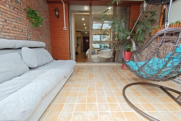 A room with a grey sofa, a hanging chair with a blue cushion, and a tiled floor.