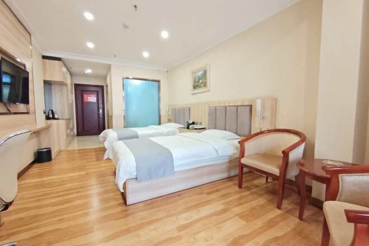 A hotel room with two beds, a wooden floor, a TV, a chair, and a desk.