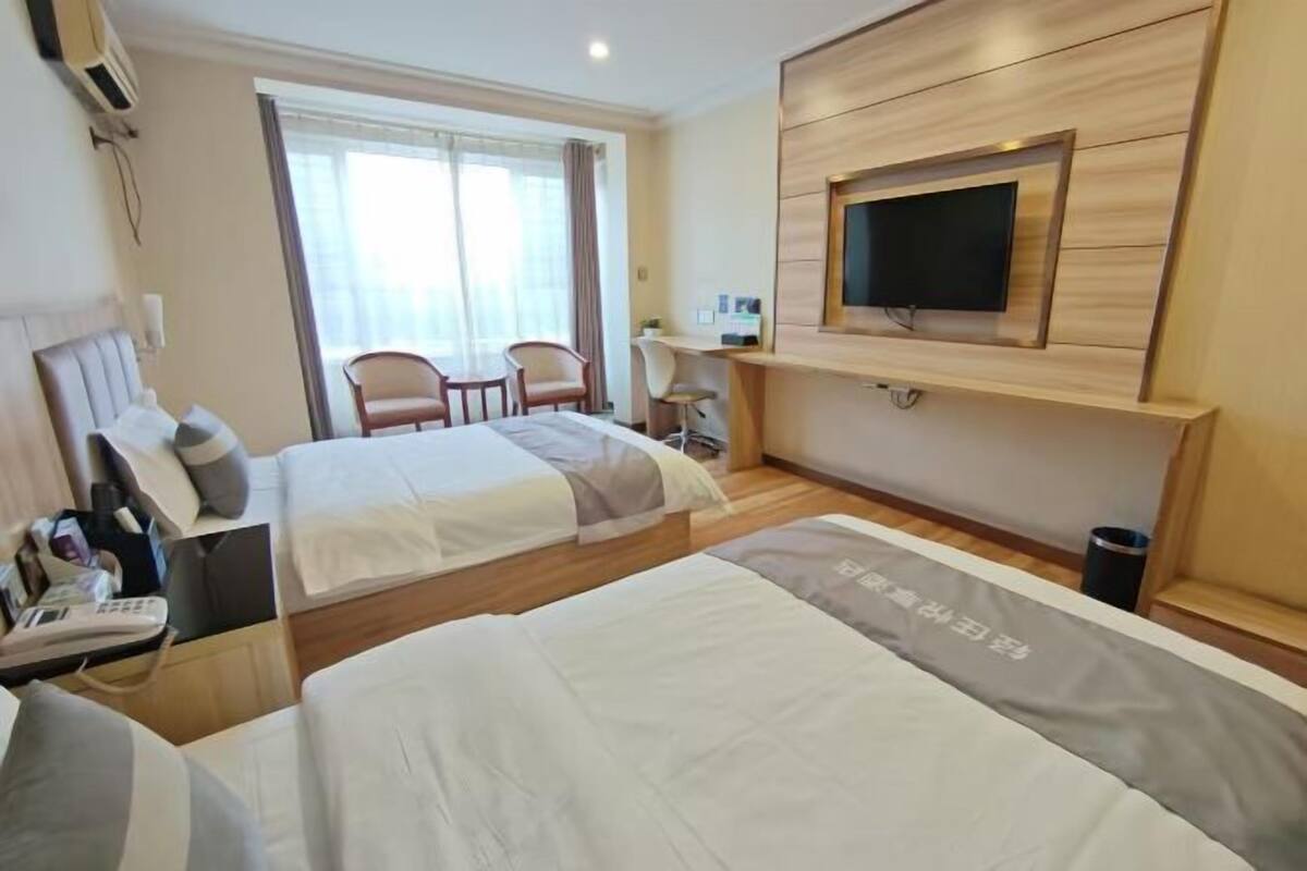 A hotel room with two beds, a TV mounted on the wall, a desk, and a chair.