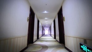 A long, narrow hotel corridor with a patterned carpet, wooden doors, and a digital exit sign.
