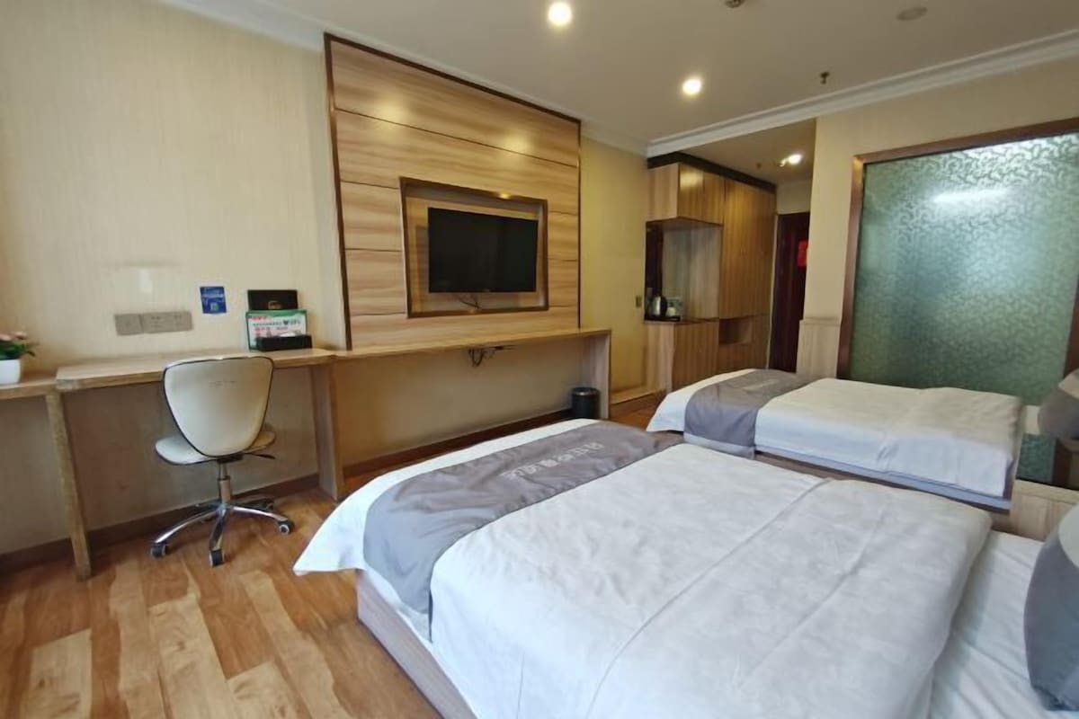 A hotel room with two beds, a desk, a chair, a TV, and a mirror.