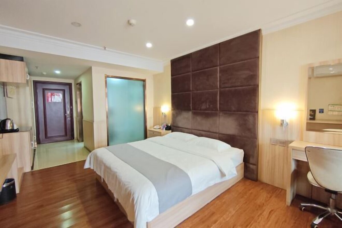 A hotel room with a large bed, a desk, a chair, a mirror, and a wardrobe.