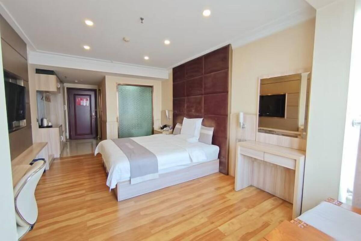 A hotel room with a large bed, a desk, a chair, a television, and a mirror.