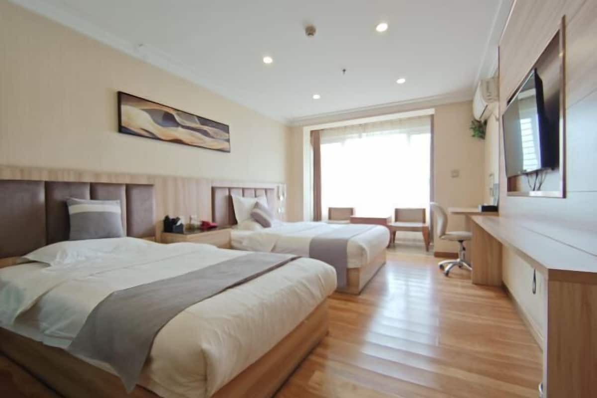 A hotel room with two beds, a desk, a chair, a TV, and a window with curtains.