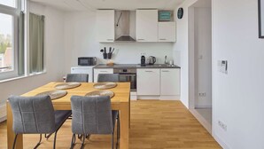 Une cuisine moderne avec des meubles blancs, une table à manger en bois et des chaises grises, ainsi qu’une fenêtre avec des rideaux.