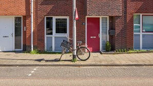 Un immeuble en briques de plusieurs étages, avec une porte rouge, un vélo garé devant et un lampadaire.