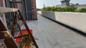 A rooftop terrace with a wooden easel, a potted plant, and a view of traditional architecture in the background. - Zaozhuang Jingxuan Inn (Zaozhuang)