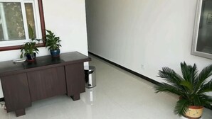A hallway with a dark wooden bench, two potted plants, a trash bin, and a framed picture on the wall. - Zaozhuang Jingxuan Inn (Zaozhuang)