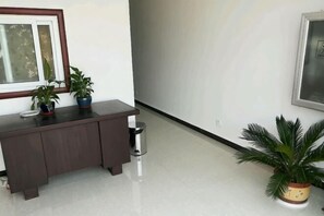 A hallway with a dark wooden bench, two potted plants, a trash bin, and a framed picture on the wall. - Zaozhuang Jingxuan Inn (Zaozhuang)