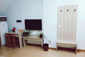Ein kleines Zimmer mit Schreibtisch, Stuhl, Fernseher und Kleiderschrank.