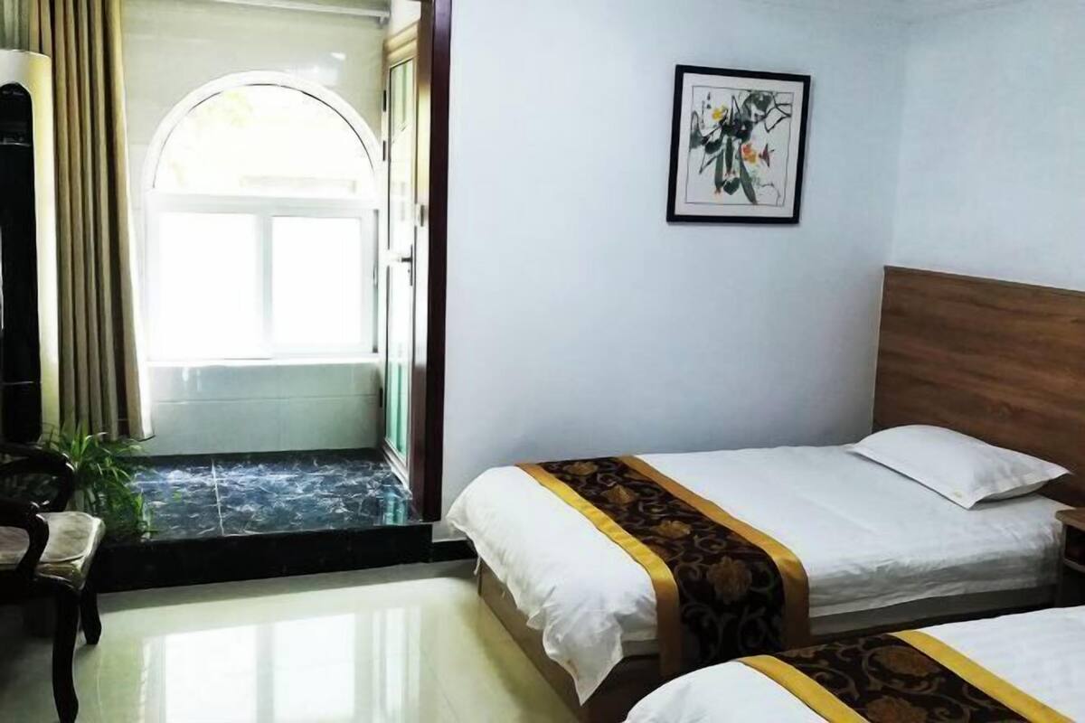 A hotel room with two beds, a framed artwork on the wall, and a view through an open door.