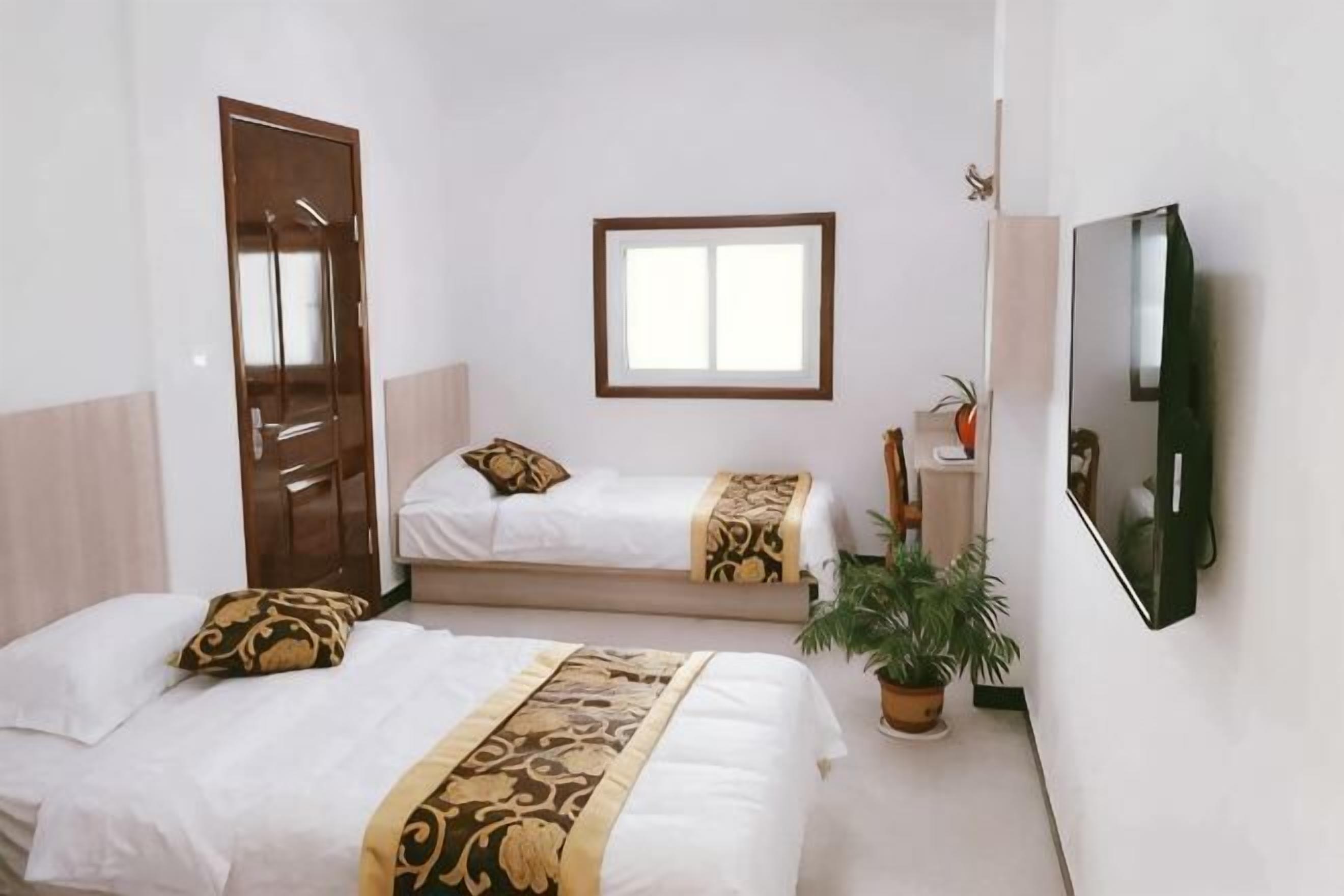 Ein Zimmer mit zwei Betten, einem Fenster, einer Tür und einem Spiegel.