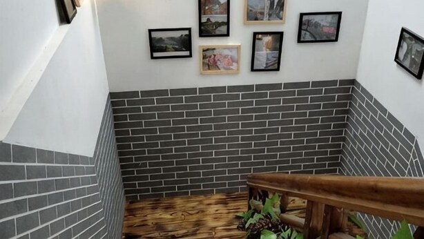 Una escalera con barandilla de madera, paredes de ladrillo gris y cuadros enmarcados.