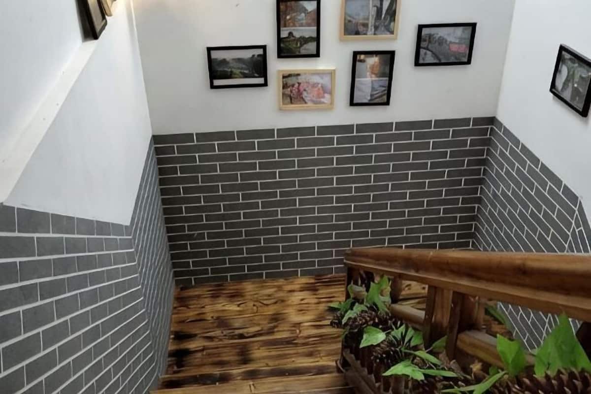 A staircase with a wooden handrail, grey brick walls, and framed pictures on the wall.