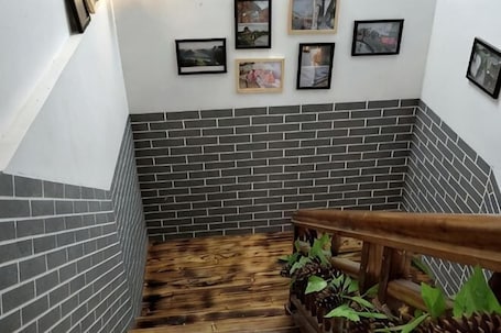 A staircase with a wooden handrail, grey brick walls, and framed pictures on the wall.. Yongzhou Ancient Village Inn
