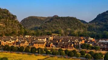 A village with traditional buildings, a clear sky, and a hilly backdrop.
