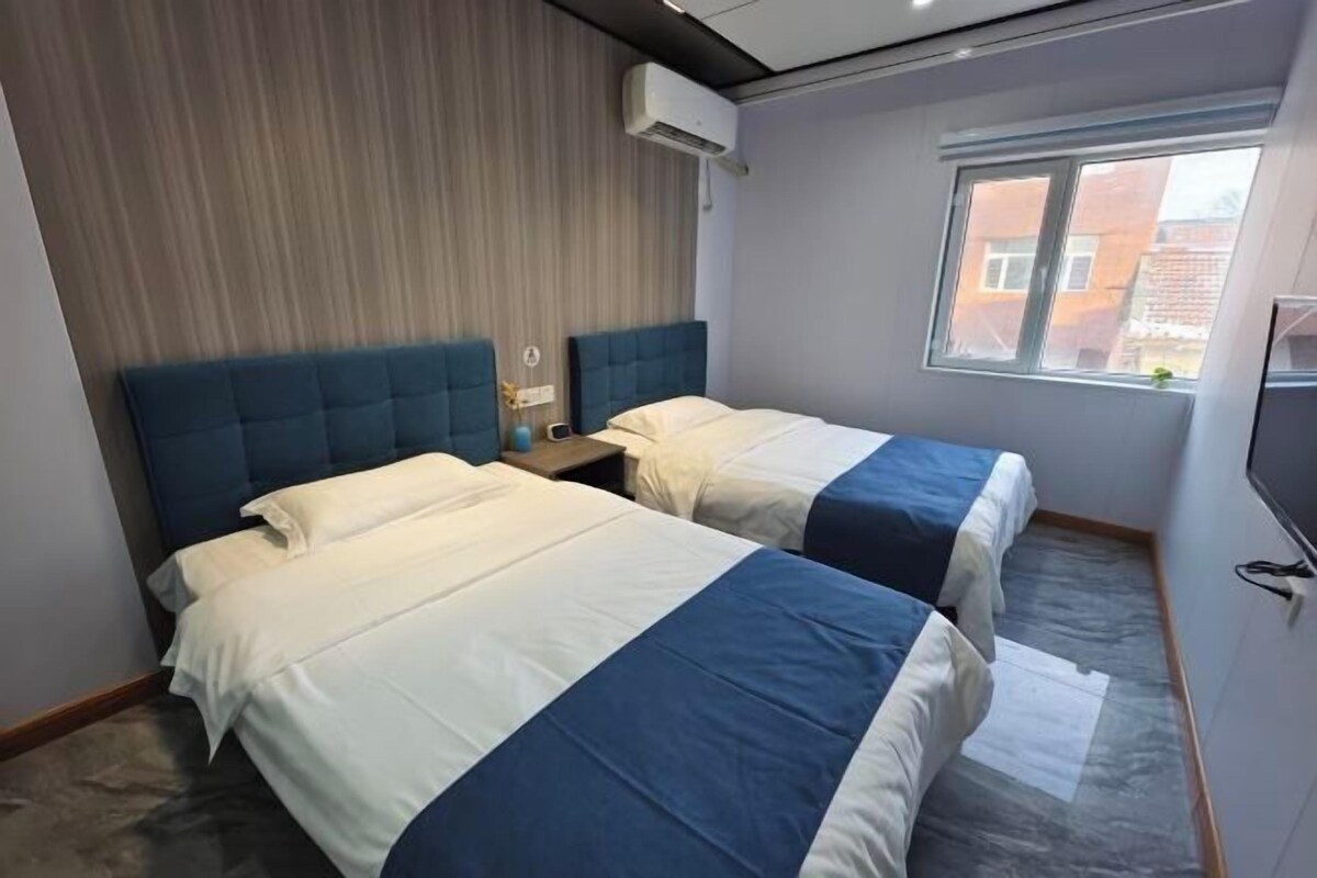 A hotel room with two beds, a window, and an air conditioning unit.