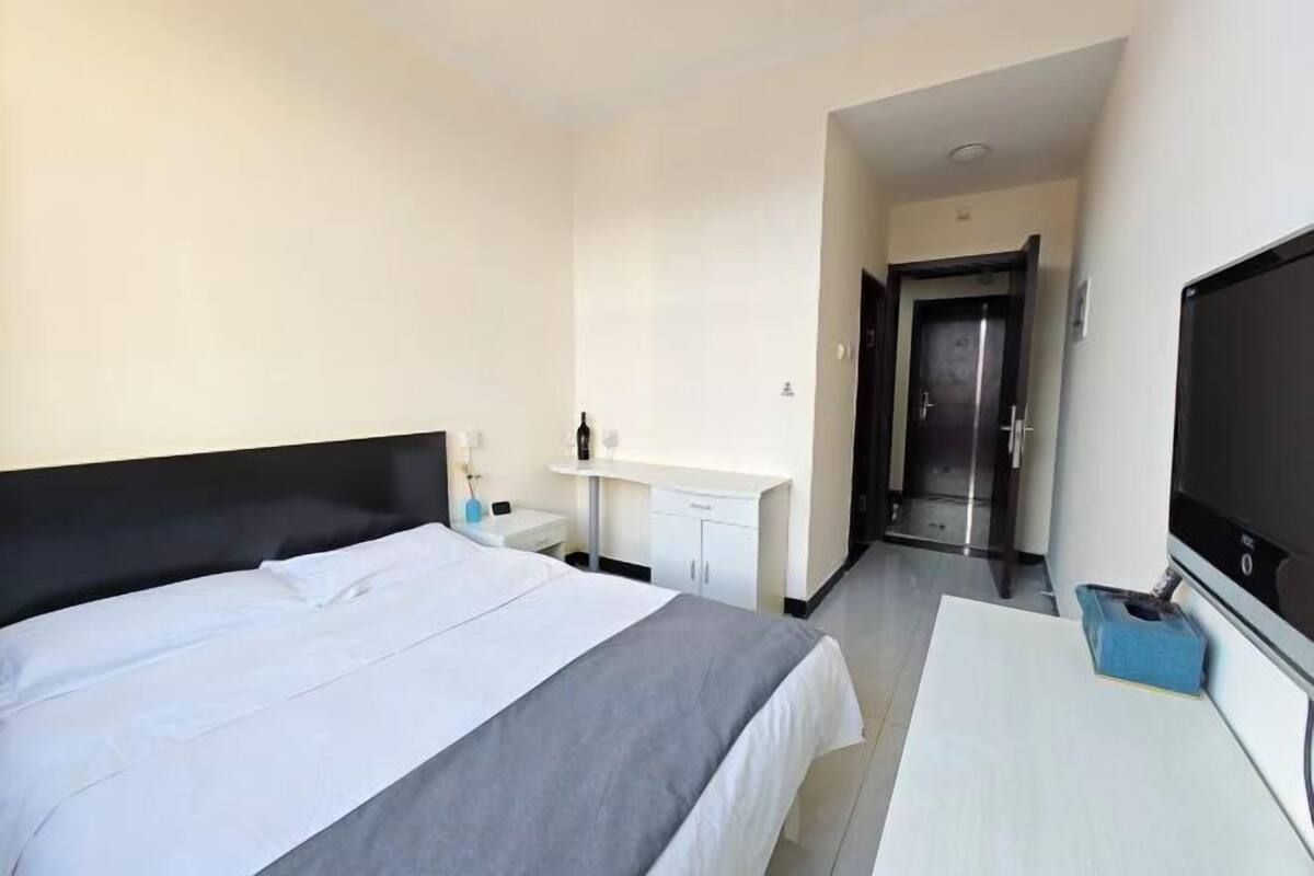 A hotel room with a bed, a desk, a TV, a bathroom, and a door.