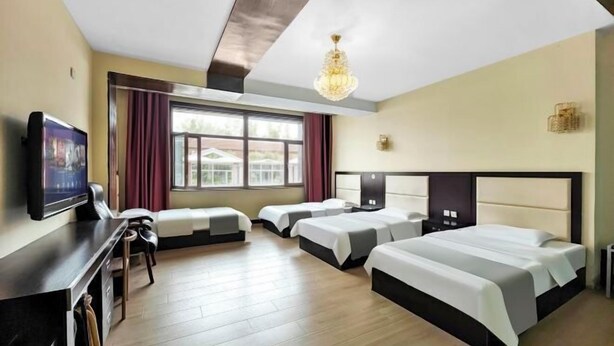 A hotel room with a large bed, two smaller beds, a desk with a chair, a TV, and a window with curtains. - Xiwuqi Jindi Hotel (West Ujimqin Banner)