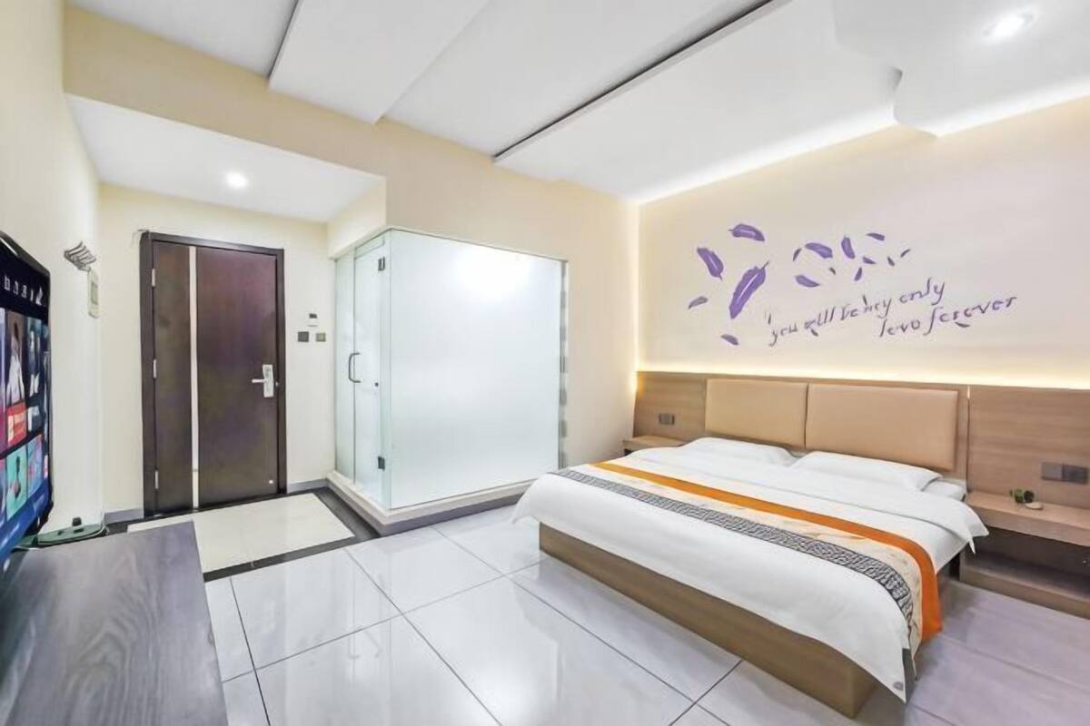 A modern hotel room with a bed, a wardrobe, a TV, and a wall with a decorative quote.